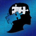 This is a puzzle of a blue background, black silhouette of a person. Two blue puzzle pieces have not been placed in the the person's head revealing a white table.