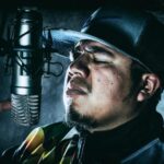 A Hispanic man speaking or singing on mic in the studio.