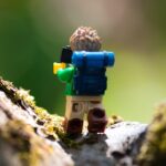 Miniature plastic hiker on a cliff edge taking a picture.