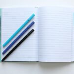 An open notebook with three blue pens.