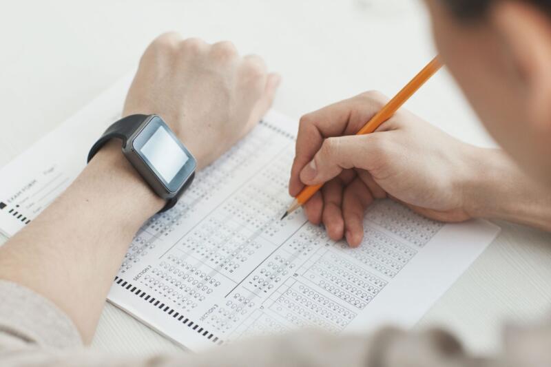 Close-up of a student writing answers on a test sheet with a pencil and smartwatch