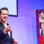 A motivational speaker standing by a PowerPoint presentation.