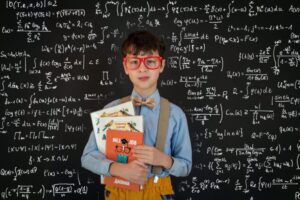 Boy standing in front of blackboard covered in mathematical equations and holding several books. Ready to give his presentation.