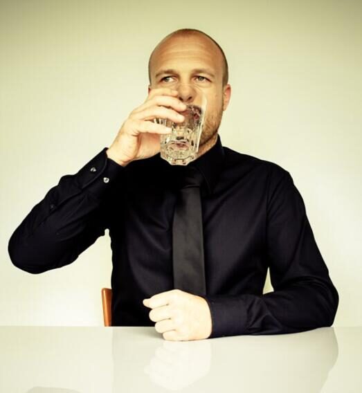 Businessman in a black shirt with a black tie drinking water.