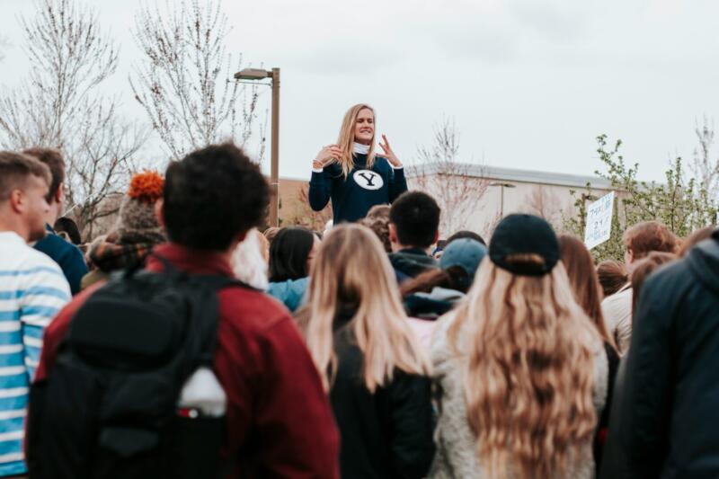 A young woman speaking confidently in front of a group of her peers.