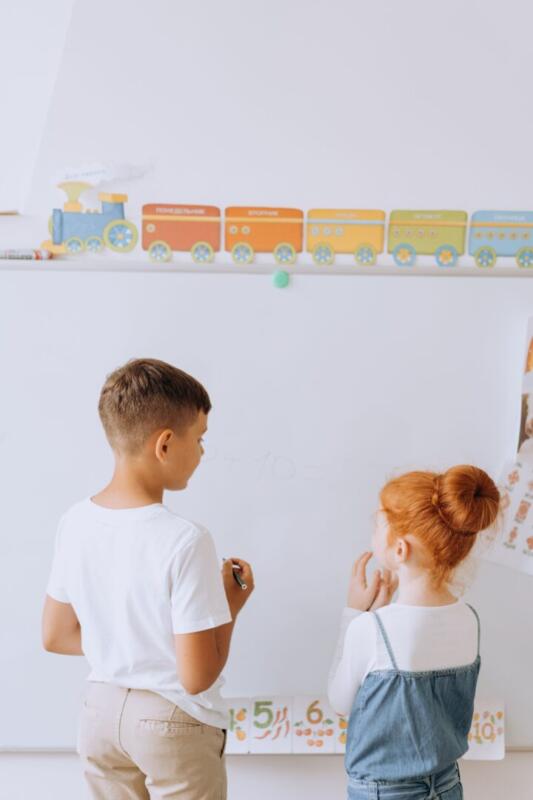 Two young children engaging in learning activities at a whiteboard in a classroom.
