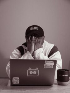 A teen with his hands over his face in academic frustration while sitting in front of his laptop computer.