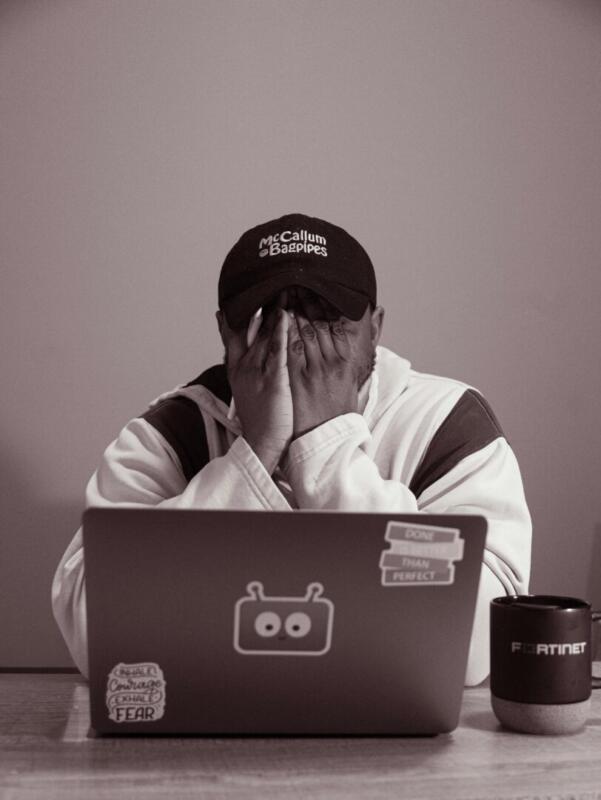A teen with his hands over his face in academic frustration while sitting in front of his laptop computer.