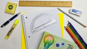 A desk top full of geometry supplies – grid paper, pencils, pen, highlighter, protractor, eraser – ready to complete homework.