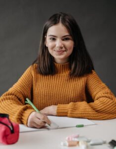 Young girl in a classroom writing with a pencil, smiling and engaged.