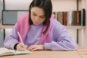Focused young woman writing notes at a library desk, working on her grid puzzles.