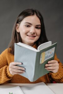 Teen girl smiling while holding a math book, showcasing her love for learning in a classroom setting.