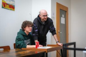Father helping his teen son to do his homework. Both are wearing hoodies.