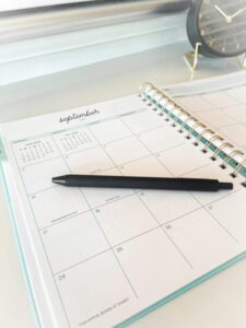 Planner Notebook/Calendar opened to September with a pen and a clock beside it.