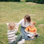 A mother reads storybooks to her children while sitting on lush green grass outdoors, fostering learning.