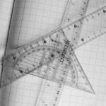 Monochrome photo of rulers and protractor on graph paper, emphasizing geometry.