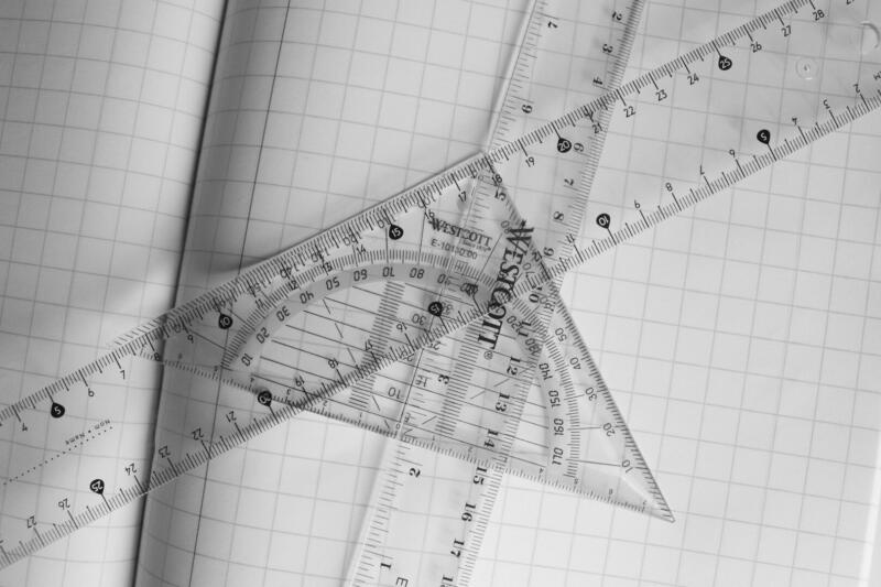Monochrome photo of rulers and protractor on graph paper, emphasizing geometry.