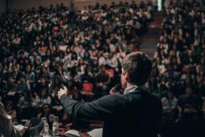 Image of a presenter addressing a blurred audience.