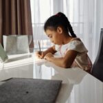 A young girl concentrates on her homework at home near a window.
