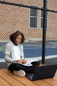 A focused girl concentrates on her homework using a laptop outdoors on a sunny day.