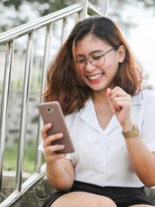Woman in white button-up shirt holding a silver iPhone. This is the feeling of happiness when having a conversation with your friend.