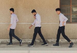 Three young men walk in sync past a simplistic urban building's facade in India. (cropped to represent the three prisoners)