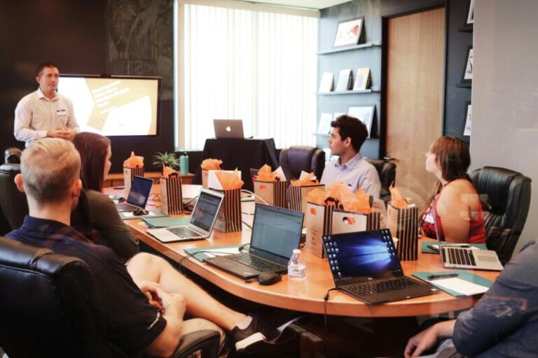 A diverse professional speaking confidently at a boardroom table with colleagues actively listening.