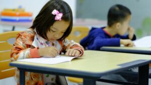 Female elementary student solving math worksheet with visual math aids for decimals.