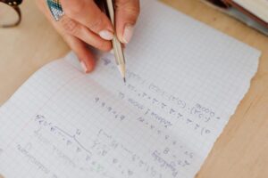 A person using order of operations as they write mathematical equations by hand on grid paper using a pencil.