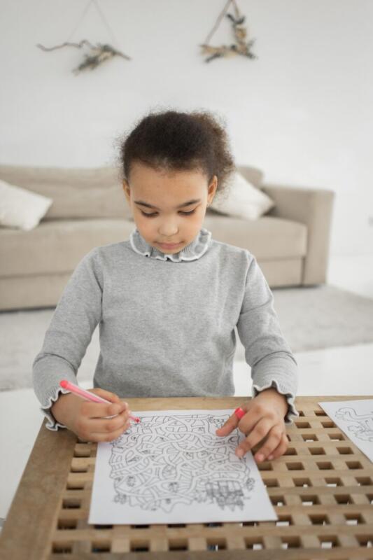 A young girl with a pencil is focused on solving a complex maze puzzle.