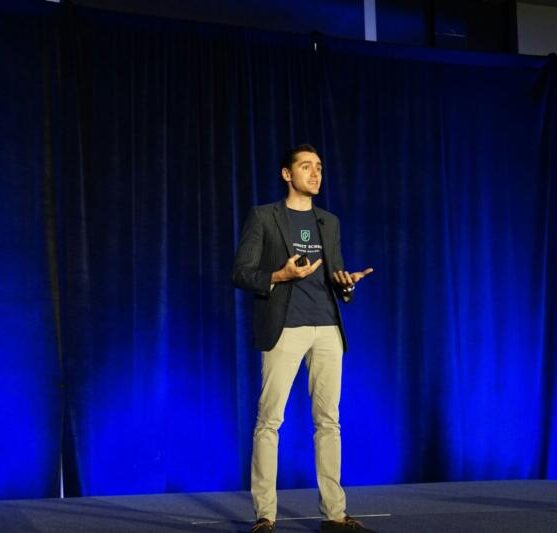 Confident speaker in front of a blue curtain on a stage.