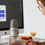 A person wearing headphones practicing speech or podcasting with a wave audio graphic on a screen.