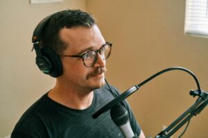 A voice actor in a soundproof recording studio wearing headphones and speaking expressively into a professional microphone.