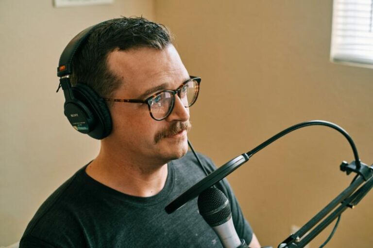 A voice actor in a soundproof recording studio wearing headphones and speaking expressively into a professional microphone.