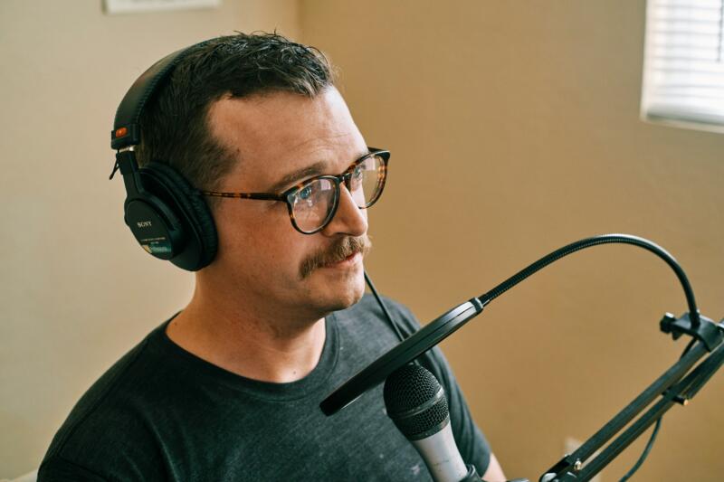 A voice actor in a soundproof recording studio wearing headphones and speaking expressively into a professional microphone.