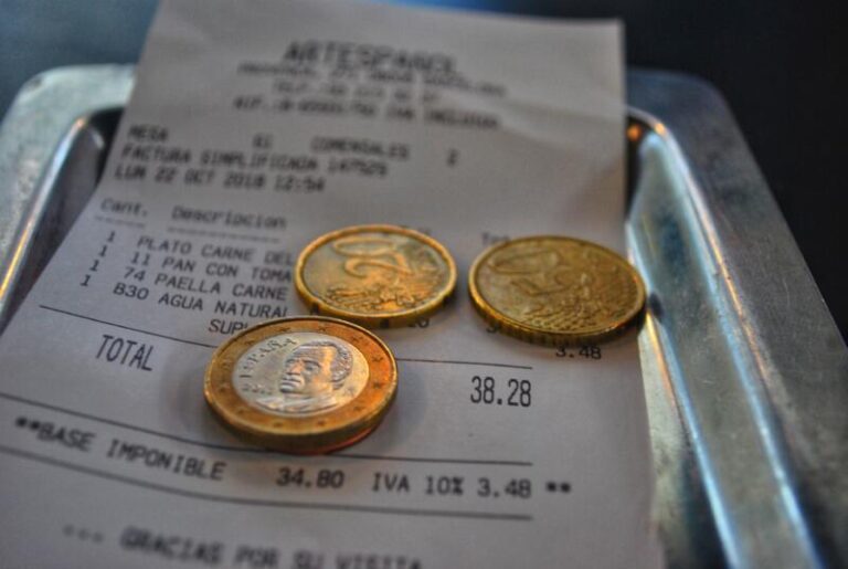 Cash dollar coins and receipt sitting on a metal receipt tray on a wooden table for math calculation