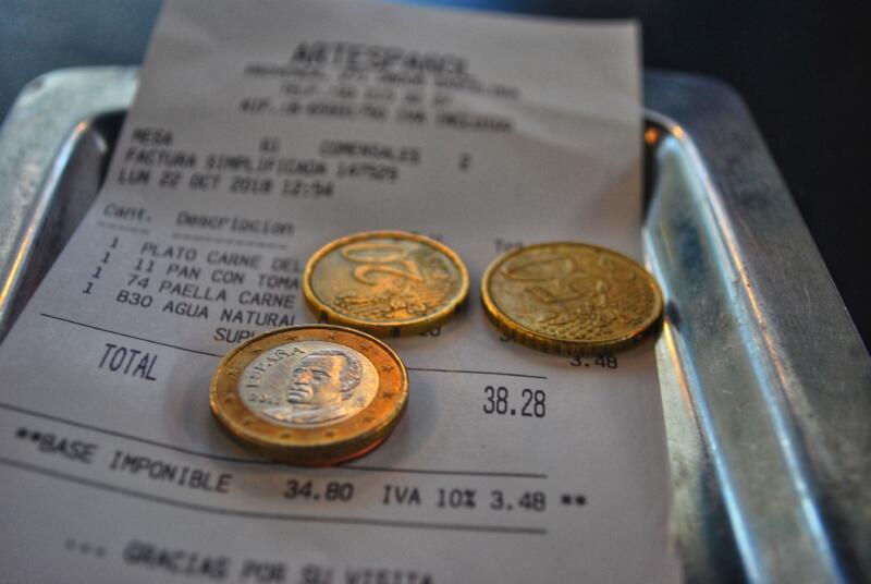 Cash dollar coins and receipt sitting on a metal receipt tray on a wooden table for math calculation