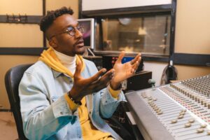 Alt Text: Studio director providing performance feedback through the recording booth glass