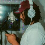 Voice actor wearing headphones holding a script at a studio recording microphone.