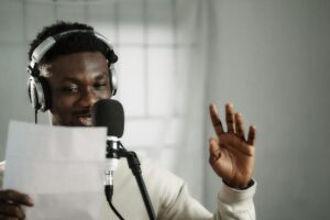 Voice actor wearing headphones and speaking into a studio condenser microphone.