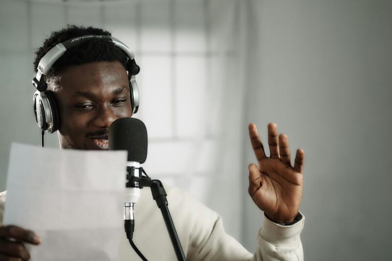 Voice actor wearing headphones and speaking into a studio condenser microphone.