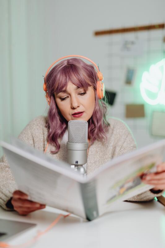 Voice actor speaking into microphone in studio booth reading commercial script.